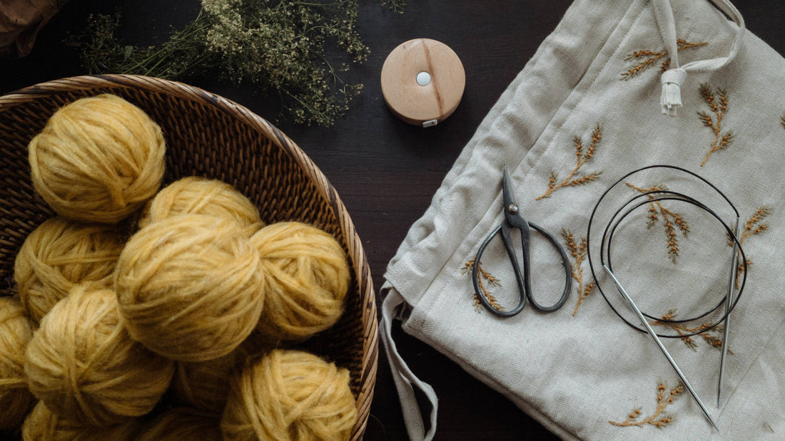 Yellow balls of unspun Nutiden yarn in a bowl, next to a pair of scissors, and needles resting on a project bag. 