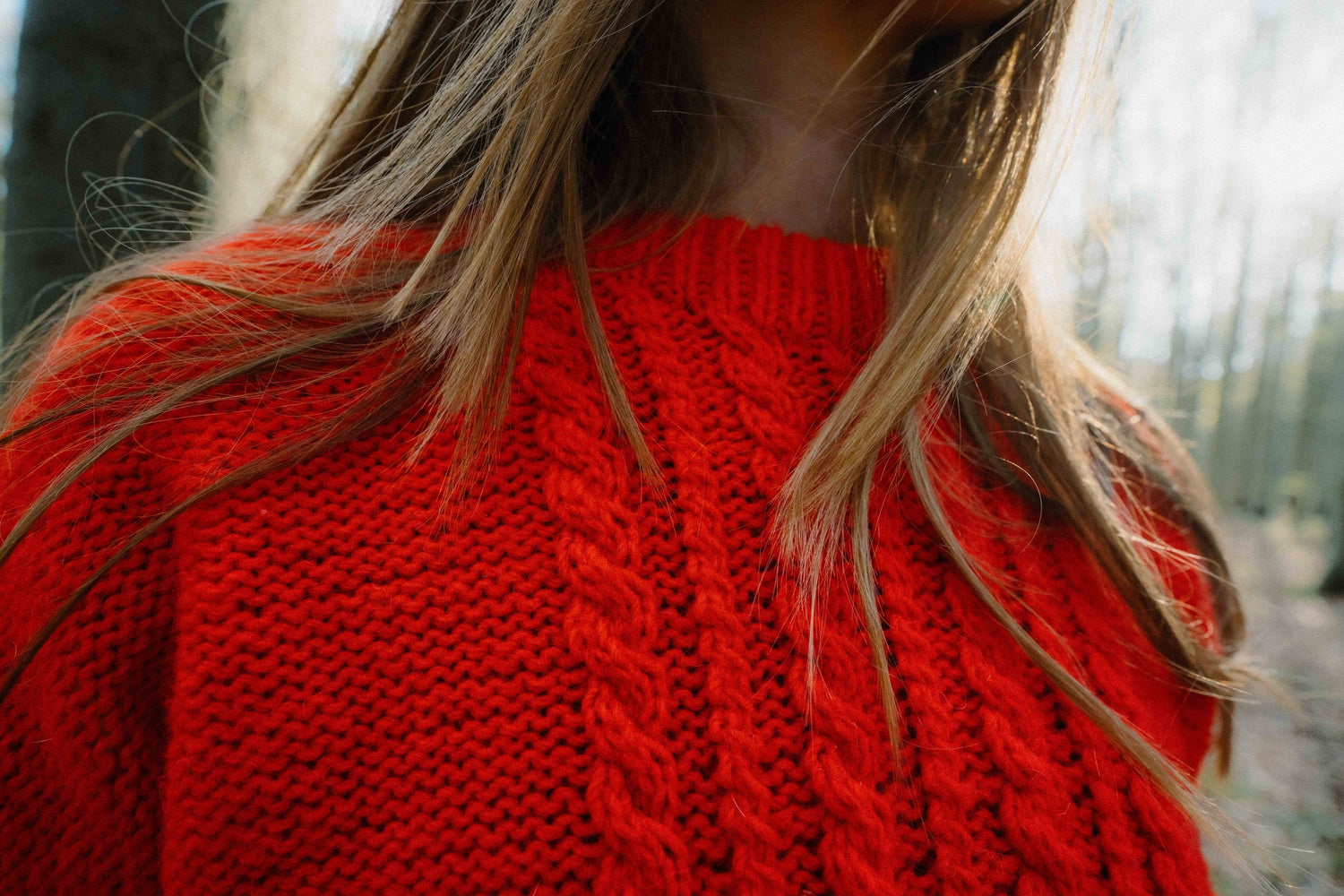 Close-up of the HELIOS SWEATER designed by Lív Ulven, highlighting the intricate cabled stitch pattern, knitted in vibrant red Mota Wooldreamers yarn.