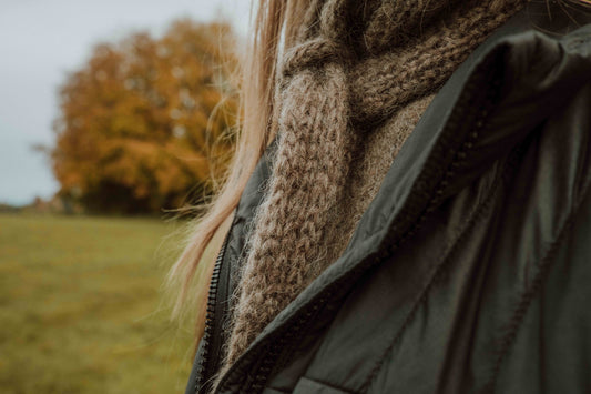 Close-up of the HAZEL SCARF, worn by designer Ulven, highlighting slip-stitch and I-cord edging, in Nutiden yarn with a blurred autumnal backdrop.