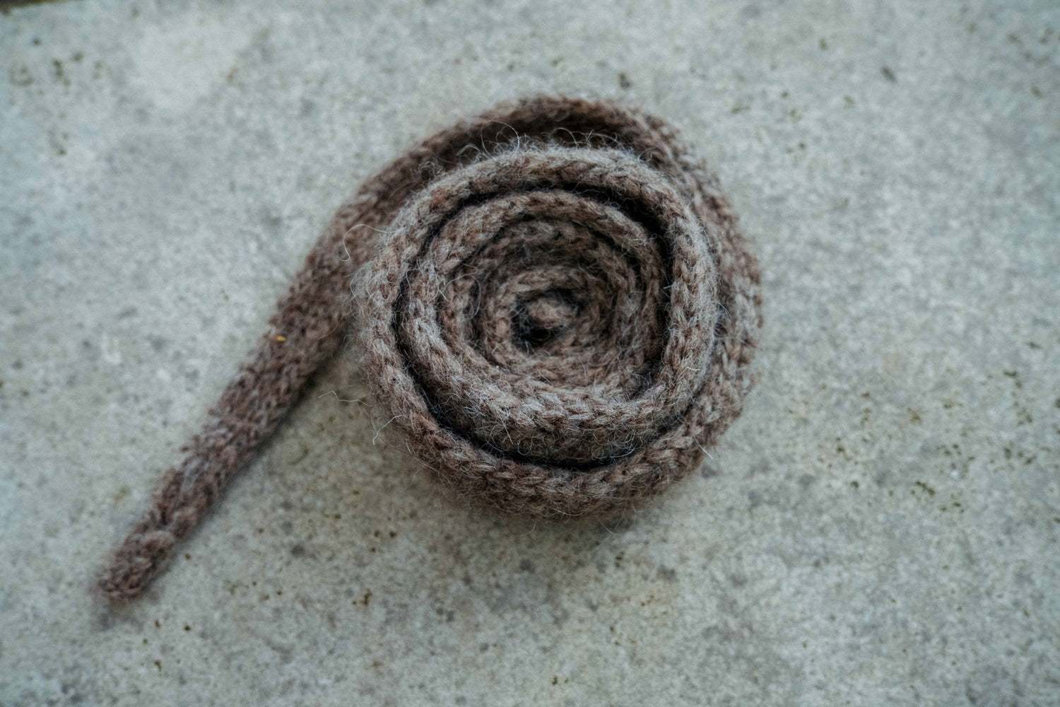 Grey-brown HAZEL SCARF with slip-stitch pattern and I-cord edge on a concrete table, knit from Nutiden yarn.