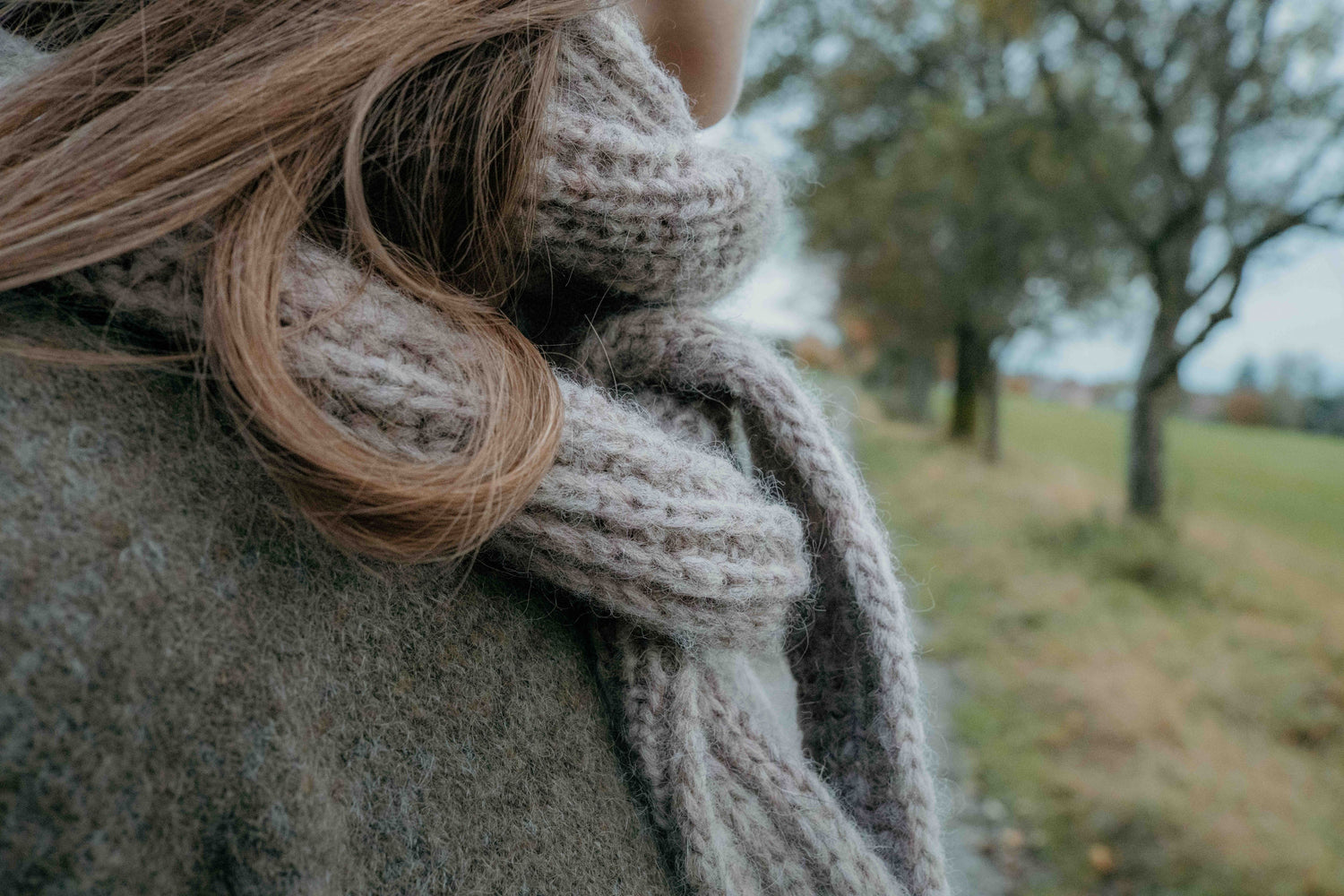 Designer Ulven wears the Season's End Shawl in a close-up that displays the half-brioche stitch and I-cord edges, knit with Höner och Eir's unspun Nutiden yarn, against a blurred autumn backdrop.